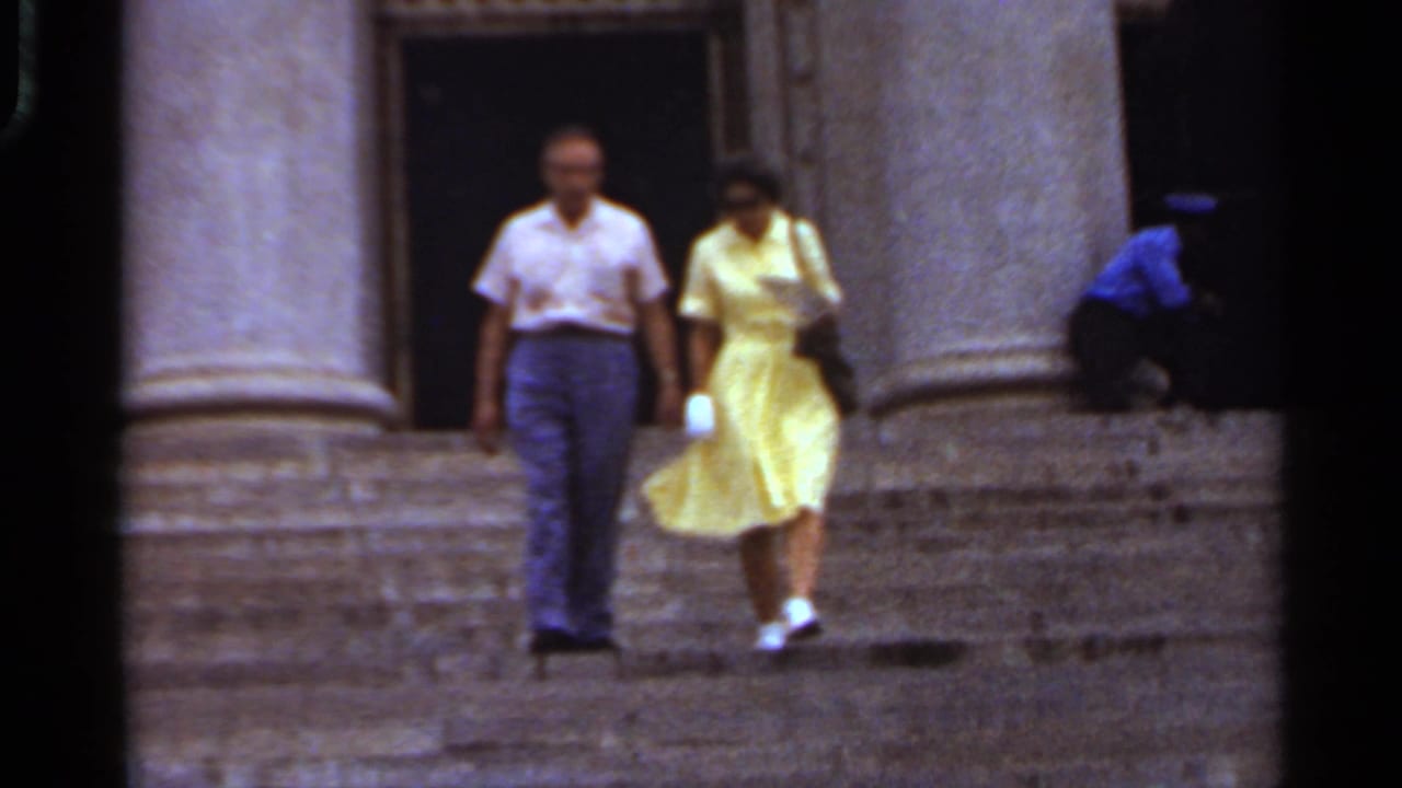 Man and woman begin walking down stone steps between large columns.