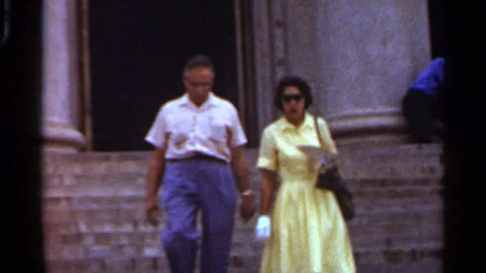 The man in a white shirt and the woman in a yellow dress come closer in the 1965 Arkansas exterior home-movie shot.