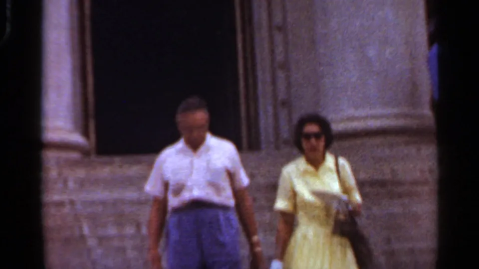 Near the end of the clip, the adults pass close to the camera on the steps, with the columned building partly out of focus behind them.