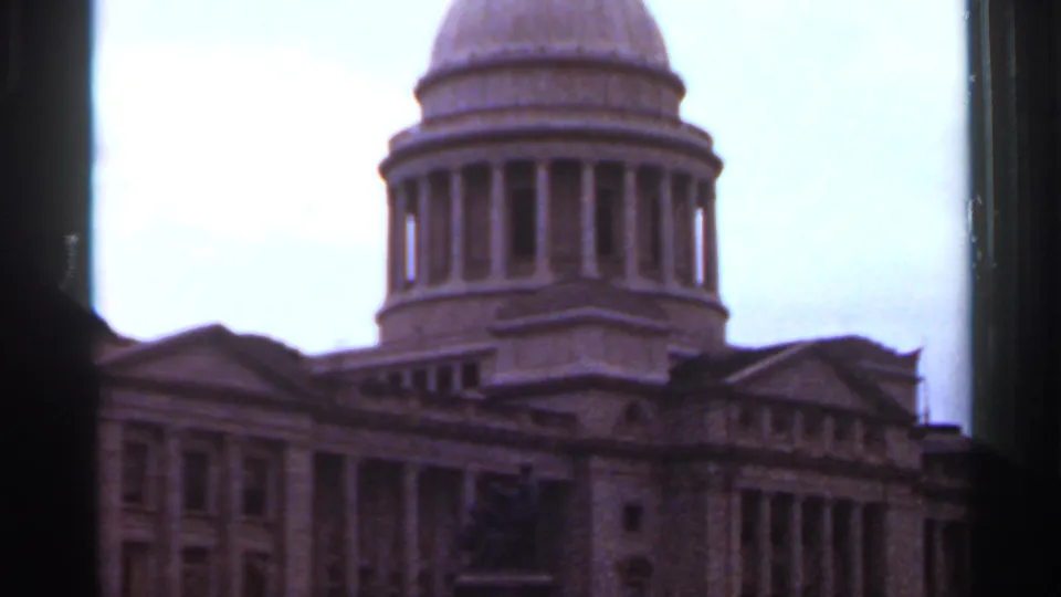 1965 8mm frame showing the Arkansas State Capitol dome and columned facade in Little Rock, softened by exposure and film grain.