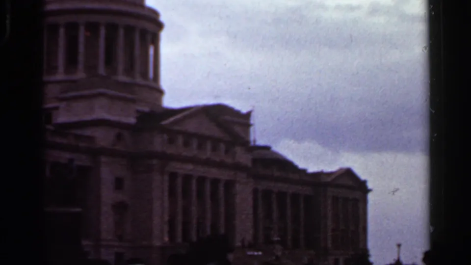 1965 Arkansas State Capitol exterior in Little Rock, seen at an angle with the dome, columns, stone facade, and cloudy sky in soft 8mm color.