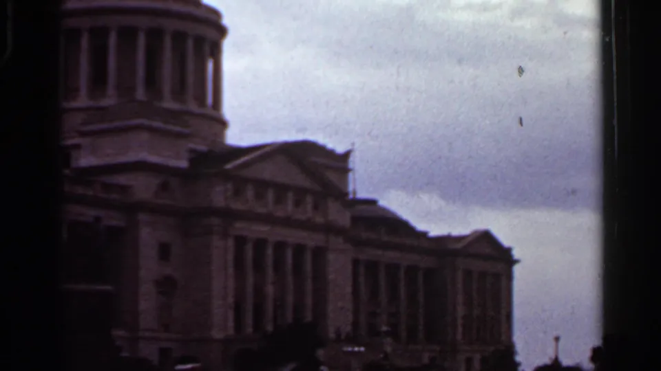 1965 Arkansas 8mm frame showing a classical domed building with columns, partly cropped by dark film borders under overcast sky.