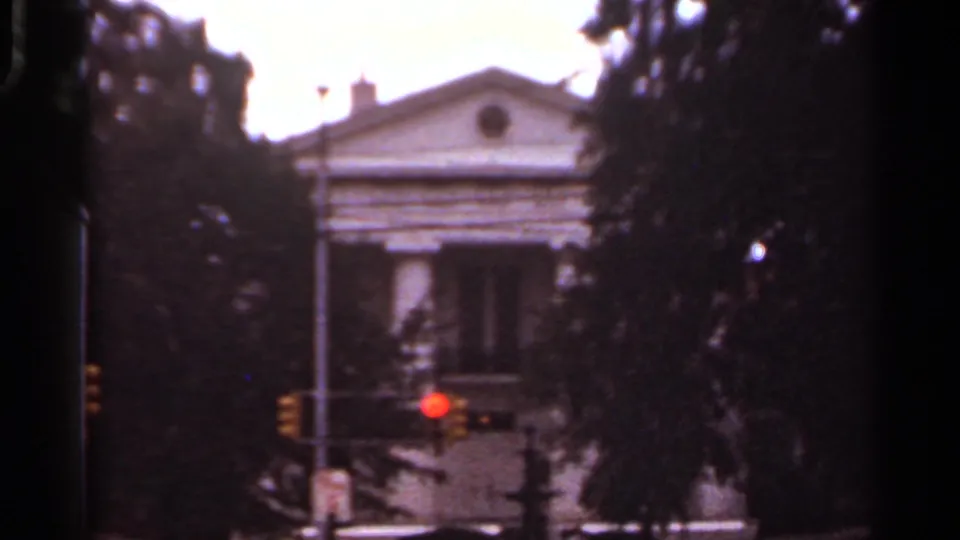 1965 Arkansas 8mm street view showing a columned facade beyond trees, with a red traffic signal in the foreground.