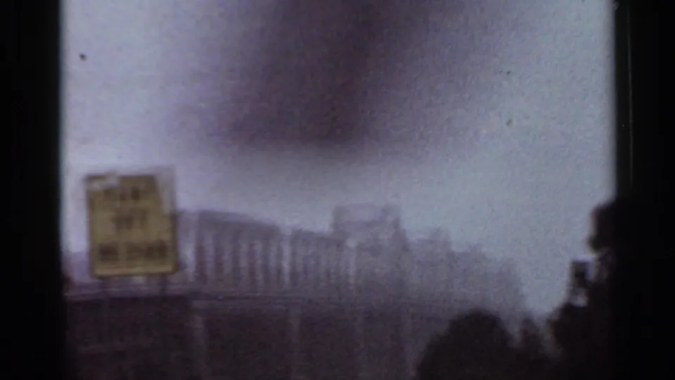 Grainy 1965 Arkansas driving view with a hazy skyline, distant buildings, roadside sign, and blurred foreground.