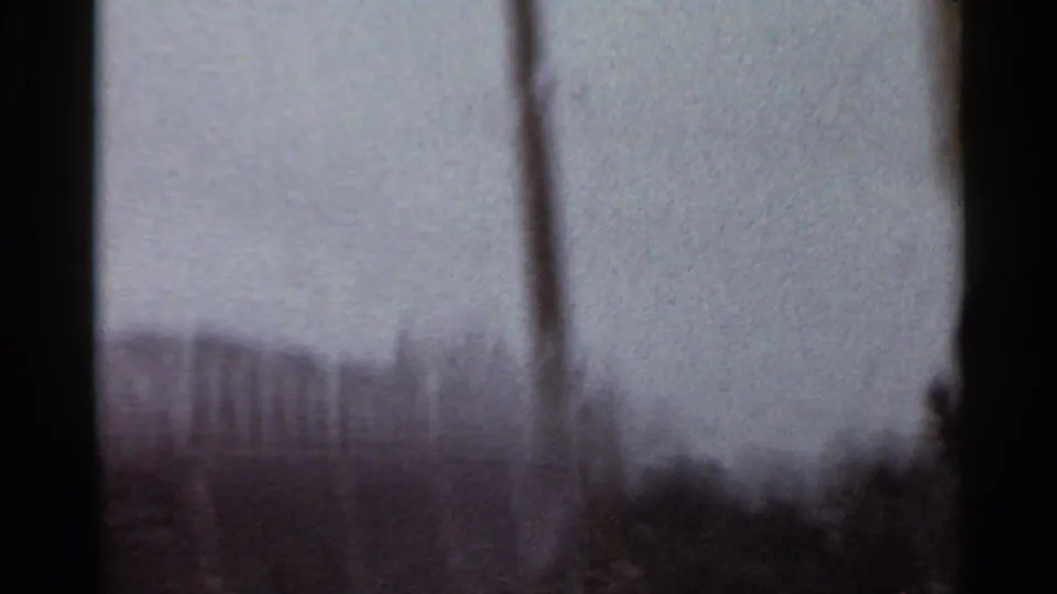 Soft, grainy 1965 Arkansas 8mm frame showing a distant city skyline, vertical pole, and dark edge of the film frame.