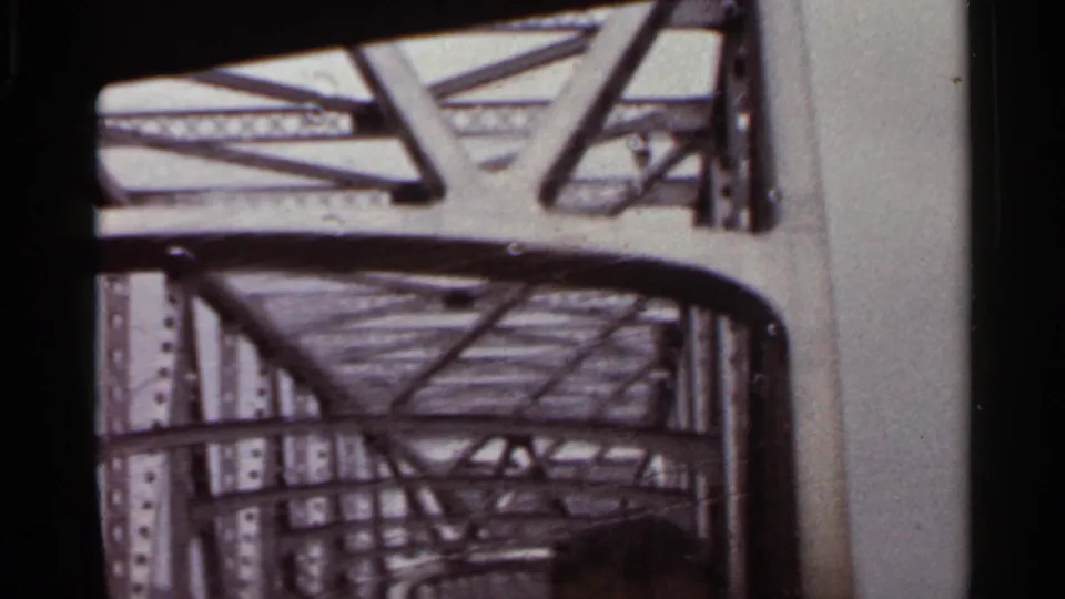 1965 Arkansas 8mm frame showing a close windshield view of riveted steel supports and overhead bridge trusses.