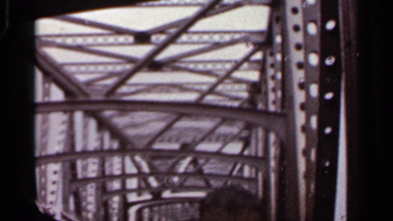 1965 Arkansas 8mm frame looking upward through riveted steel bridge beams as a car passes underneath.