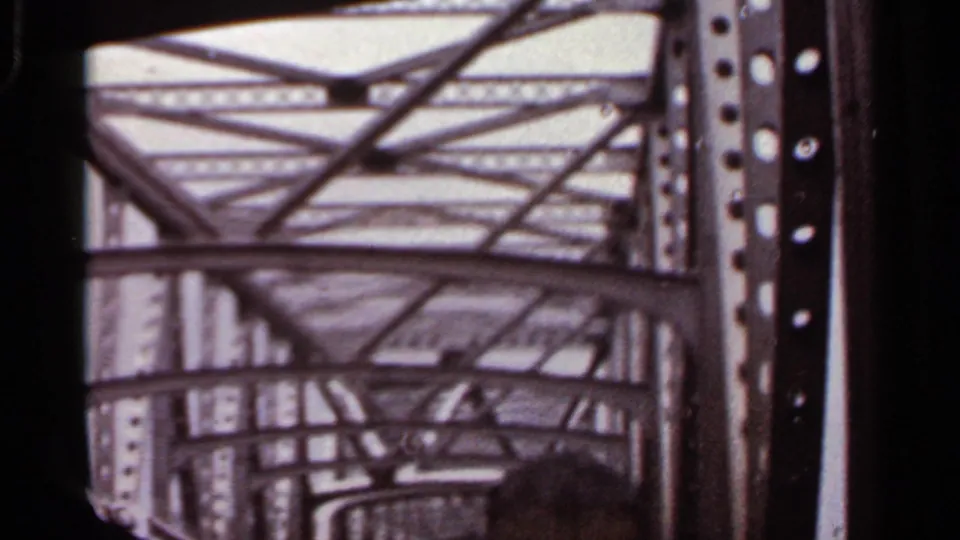 1965 Arkansas 8mm frame looking upward through riveted steel bridge beams as a car passes underneath.