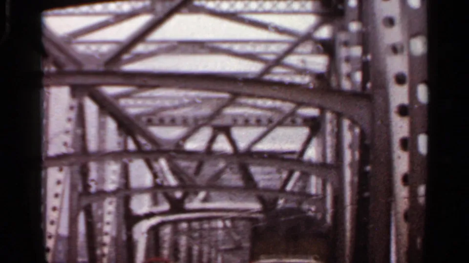 Home-movie view from beneath a large Arkansas metal truss bridge, with riveted columns and curved supports visible.