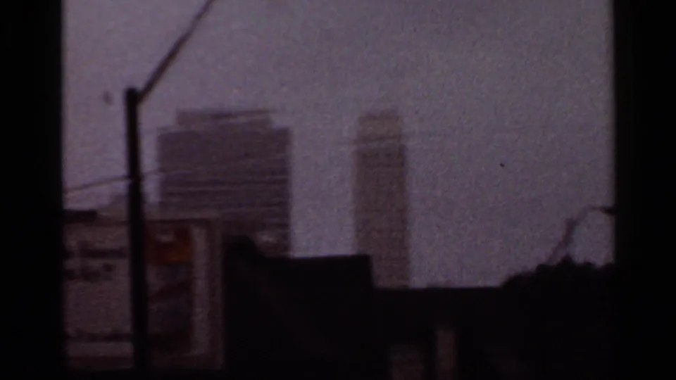 1965 Arkansas 8mm frame with distant buildings, utility poles, and bridge-edge darkness seen from a moving vehicle.