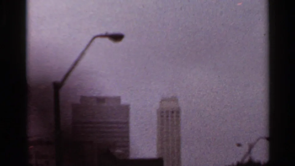 1965 Arkansas 8mm frame looking through wet vehicle glass toward a streetlamp and indistinct tall downtown buildings.