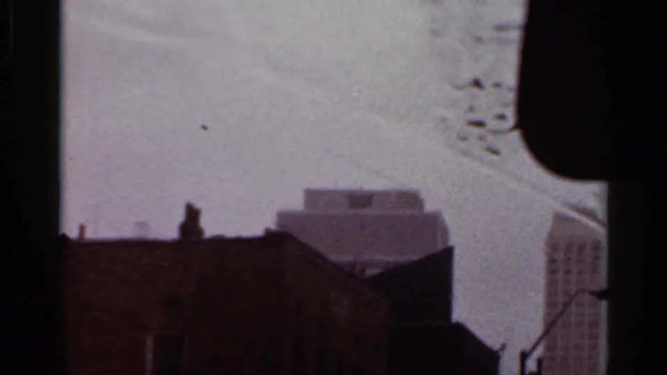 Rainy 8mm view from a vehicle in Arkansas, with a dark rooftop foreground and softened downtown buildings beyond.
