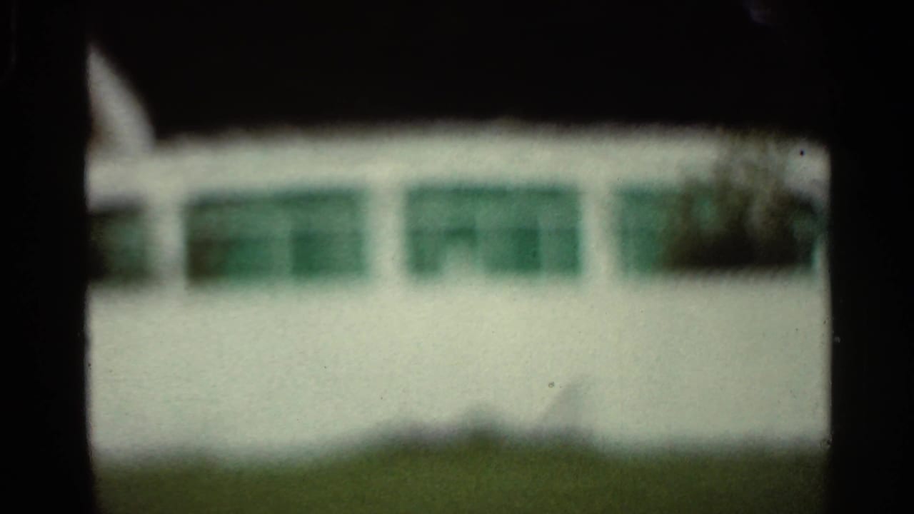 Soft-focus white building with green window panels behind dark film-frame edges.