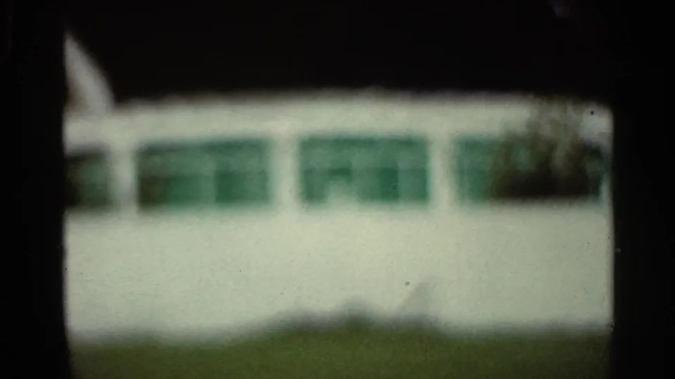 1965 Arkansas 8mm frame showing a blurry pale building with green windows, grass below, and heavy dark border exposure.