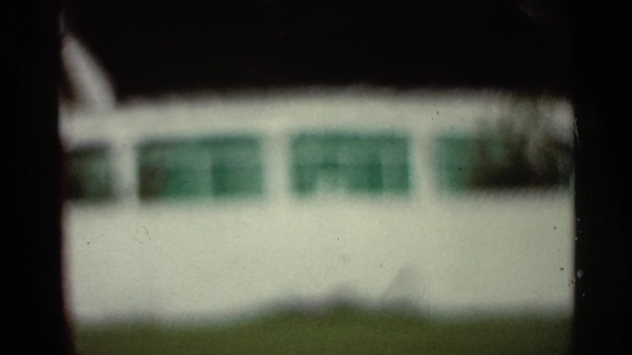 Blurred white structure with green windows and dark vertical frame edges.