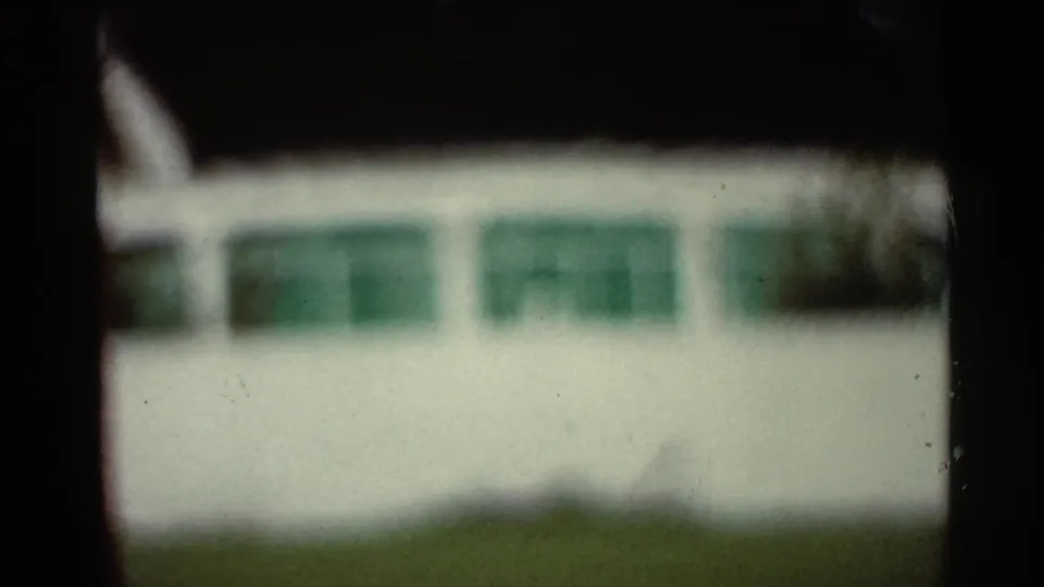 Out-of-focus 1965 Arkansas home-movie view of a pale exterior wall with green rectangular windows and dark gate edges.