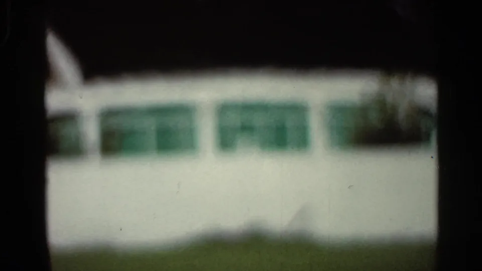 Soft 8mm frame from Arkansas in 1965 showing a pale building facade, green windows, grass, and pronounced dark framing.