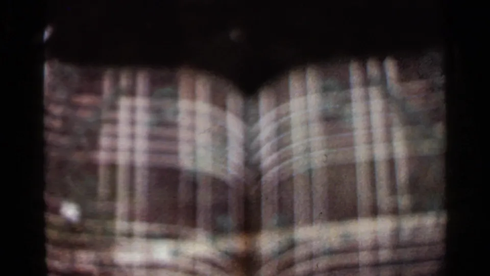 Blurred 1965 Arkansas 8mm frame with film overlap, showing a tan arched facade and a dark metal fountain shape.