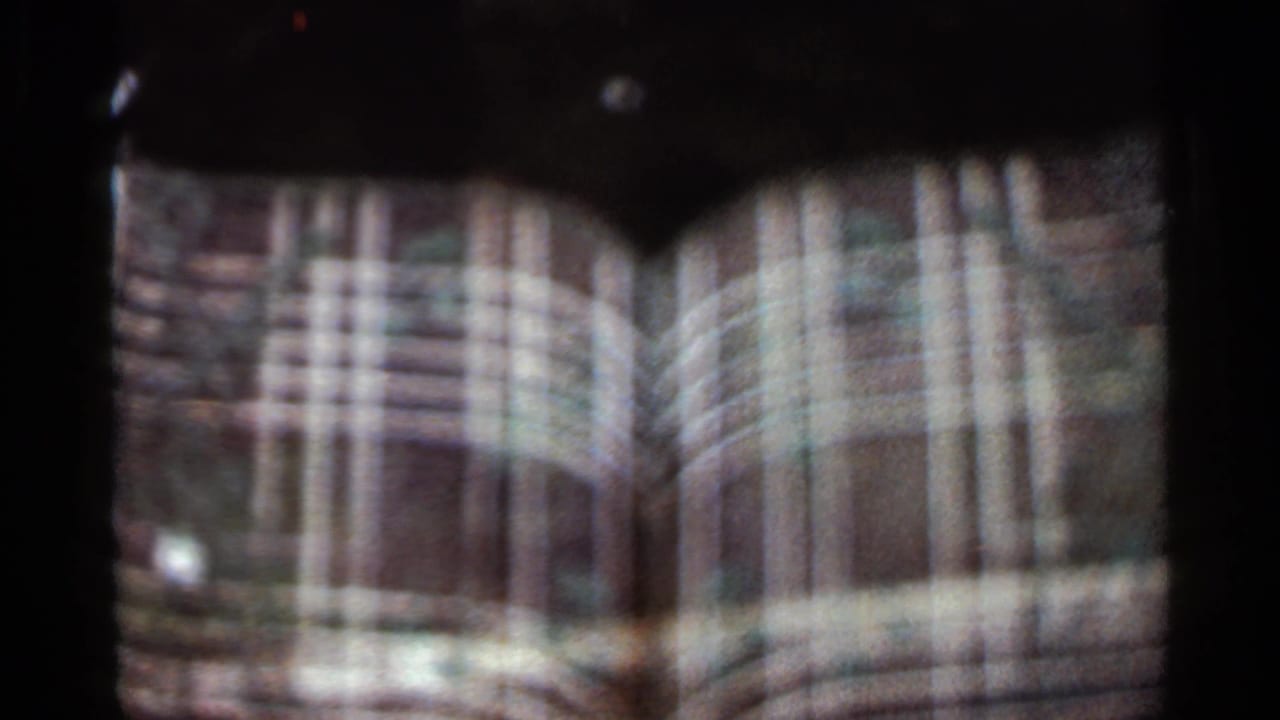 Soft 8mm view of a tan arched building facade with a dark fountain shape below.