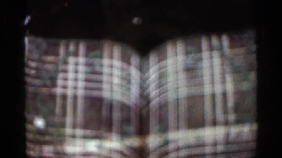 1965 Arkansas home-movie frame shows a tan masonry facade with arched windows and a dark metal fountain shape in soft focus.