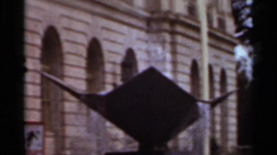 Clearer 1965 Arkansas 8mm frame of a dark metal fountain set before a tan building facade with arched windows.