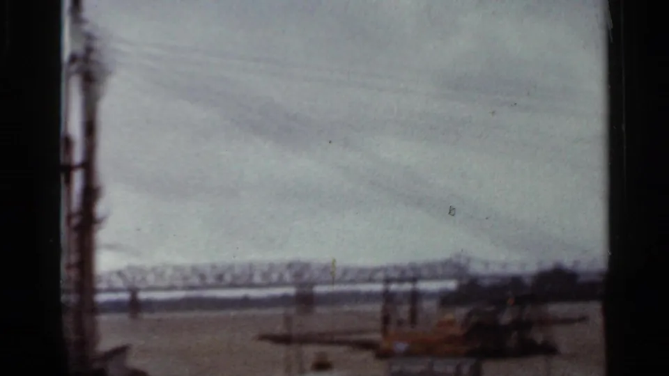 1965 Arkansas 8mm frame from a moving train, looking across a wide river toward a steel truss bridge and distant tree line.