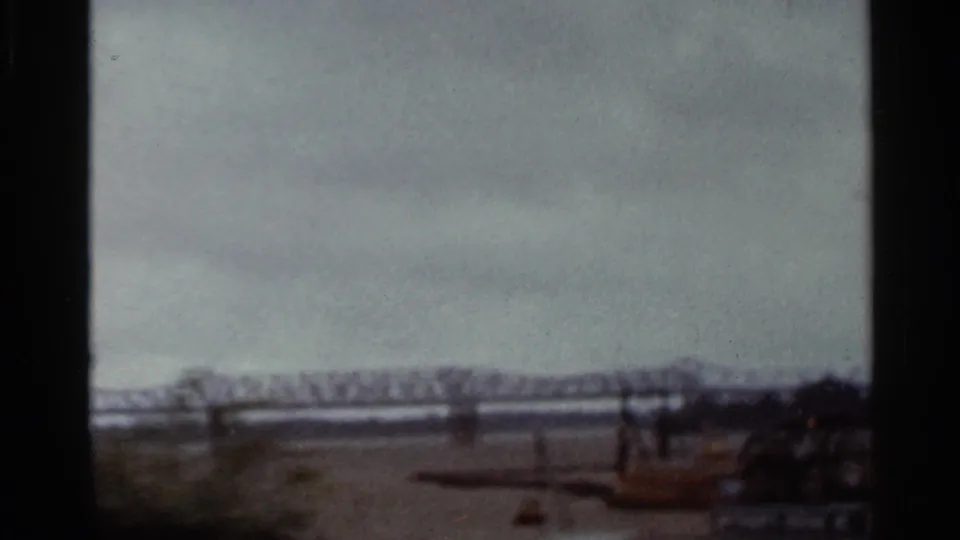 1965 Arkansas 8mm frame showing a distant steel truss bridge across a broad river, viewed through train-side framing.