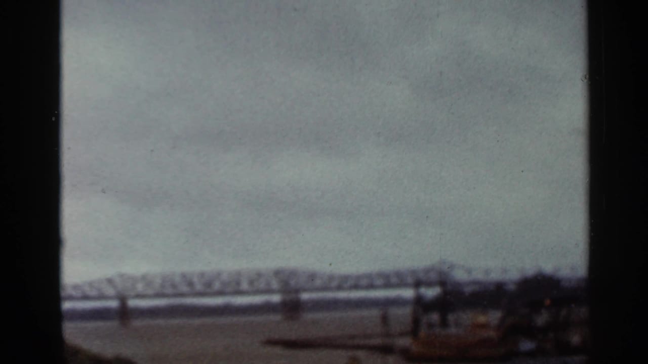 1965 Arkansas 8mm frame showing a distant steel truss bridge spanning water under heavy cloud cover.