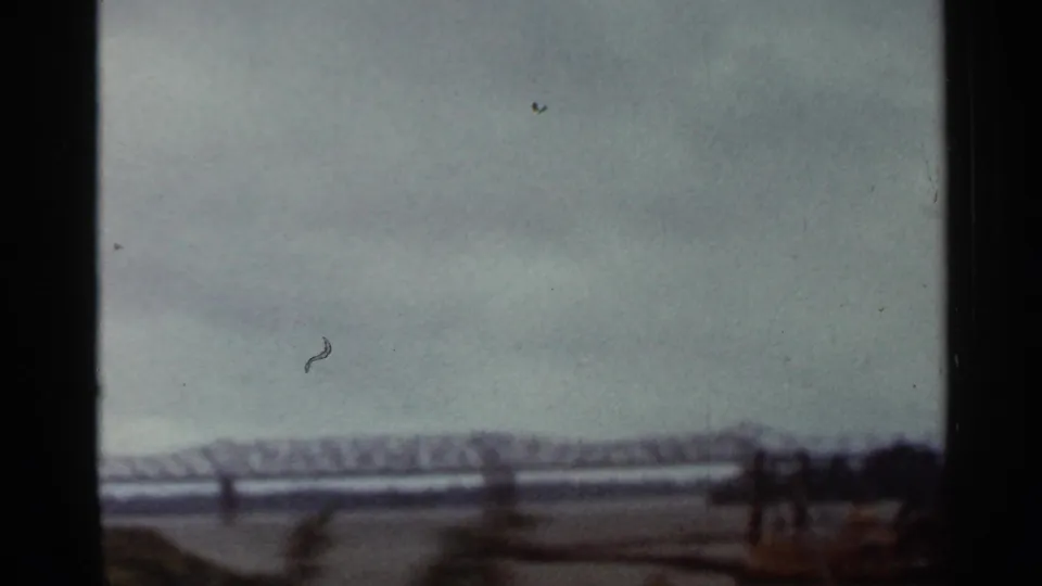 Distant Arkansas bridge view on 8mm film, with the truss line crossing water below a gray sky.