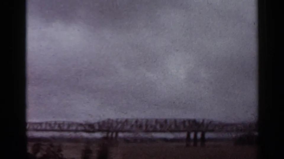 Arkansas 1965 8mm frame showing the bridge more clearly across the lower frame, with water and a heavy sky behind it.