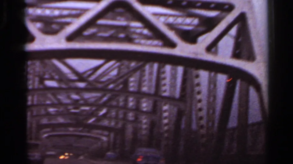 Inside-car 1965 Arkansas view looking through steel bridge girders, with dark vehicle framing and faint lights below.