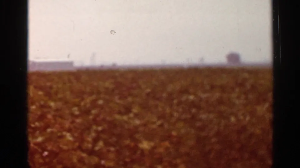 Soft 8mm frame from the St. Louis, Missouri sequence showing a reddish field, bright sky, and indistinct structure on the horizon.