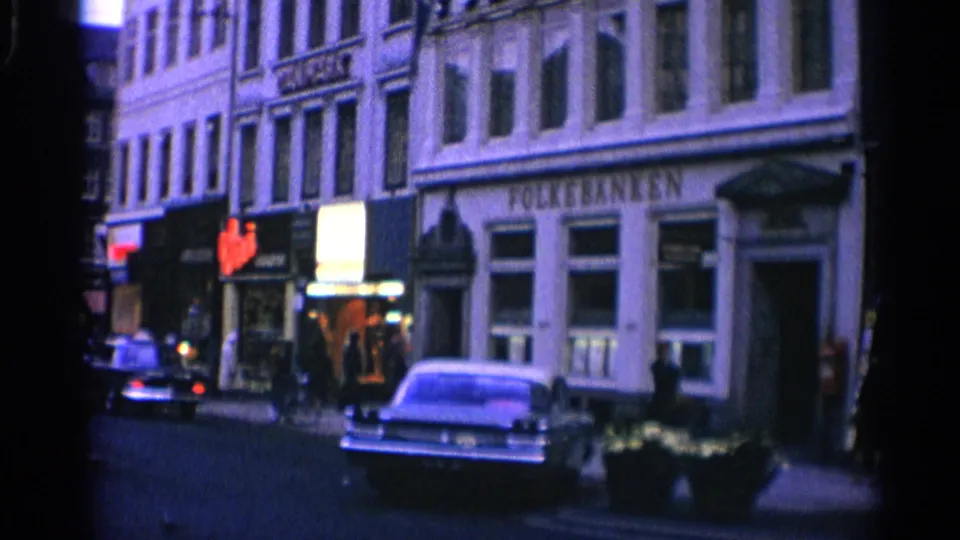 1965 Copenhagen street view showing Folke Banken, a parked mid-century car, pedestrians, and neighboring storefronts on an older city block.