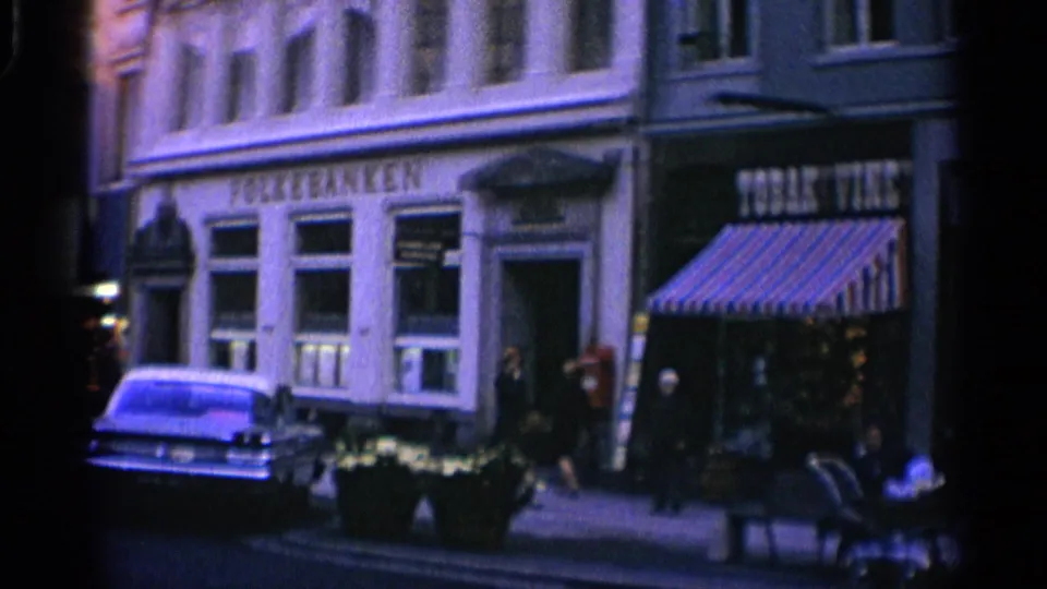 1965 Copenhagen downtown facade with Folke Banken signage, Tobac Vine storefront, pedestrians near the sidewalk, and a parked period car.