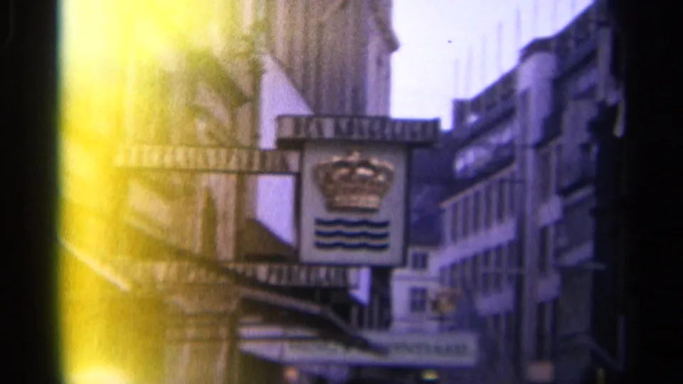 1965 Copenhagen street detail with a crowned Da Konge sign, projecting shop awnings, older building facades, and bright film flare at the edge.