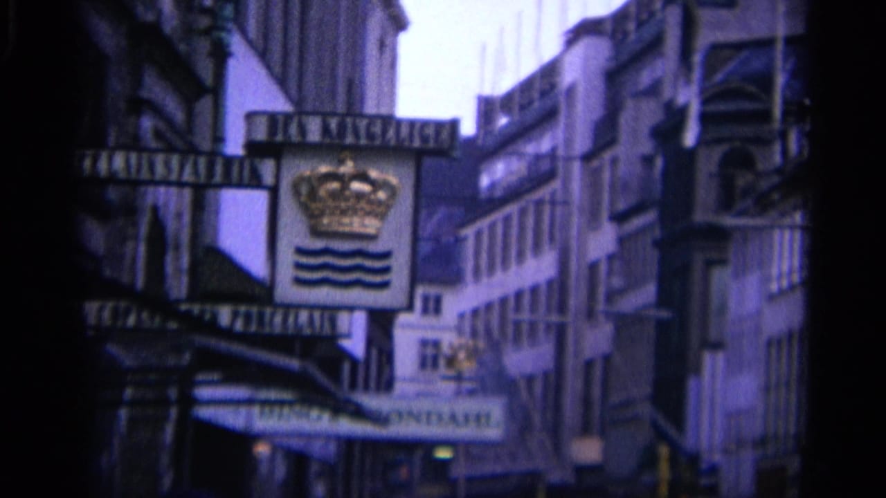 Crown-and-waves sign hanging above a narrow city street with buildings and awnings.