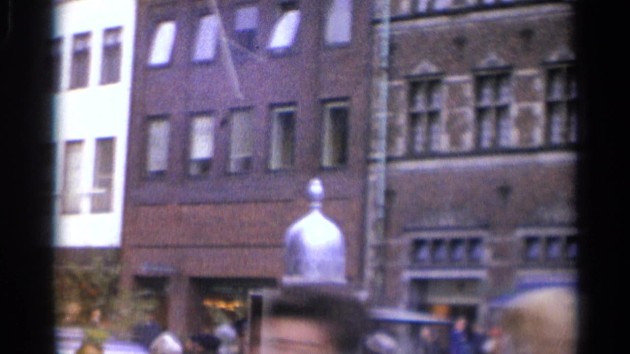 1965 Copenhagen street view with brick building fronts, blurred pedestrians, and a small white structure topped by a silver dome.