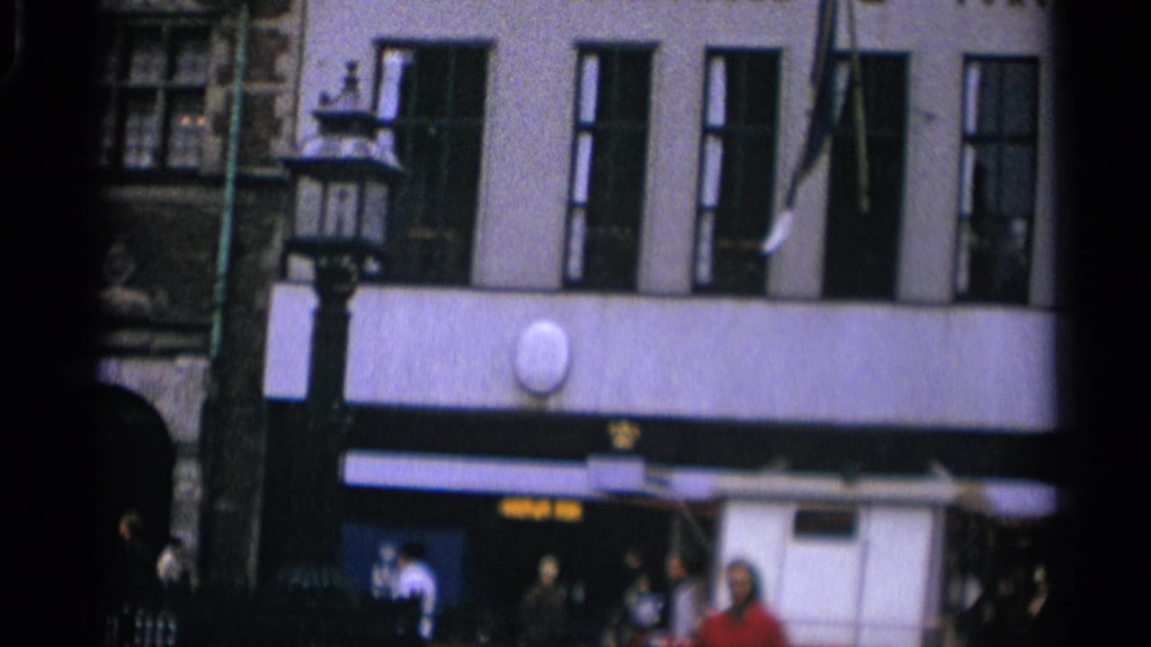 Pale multi-story building with tall windows, street lamp, awnings, and pedestrians below.
