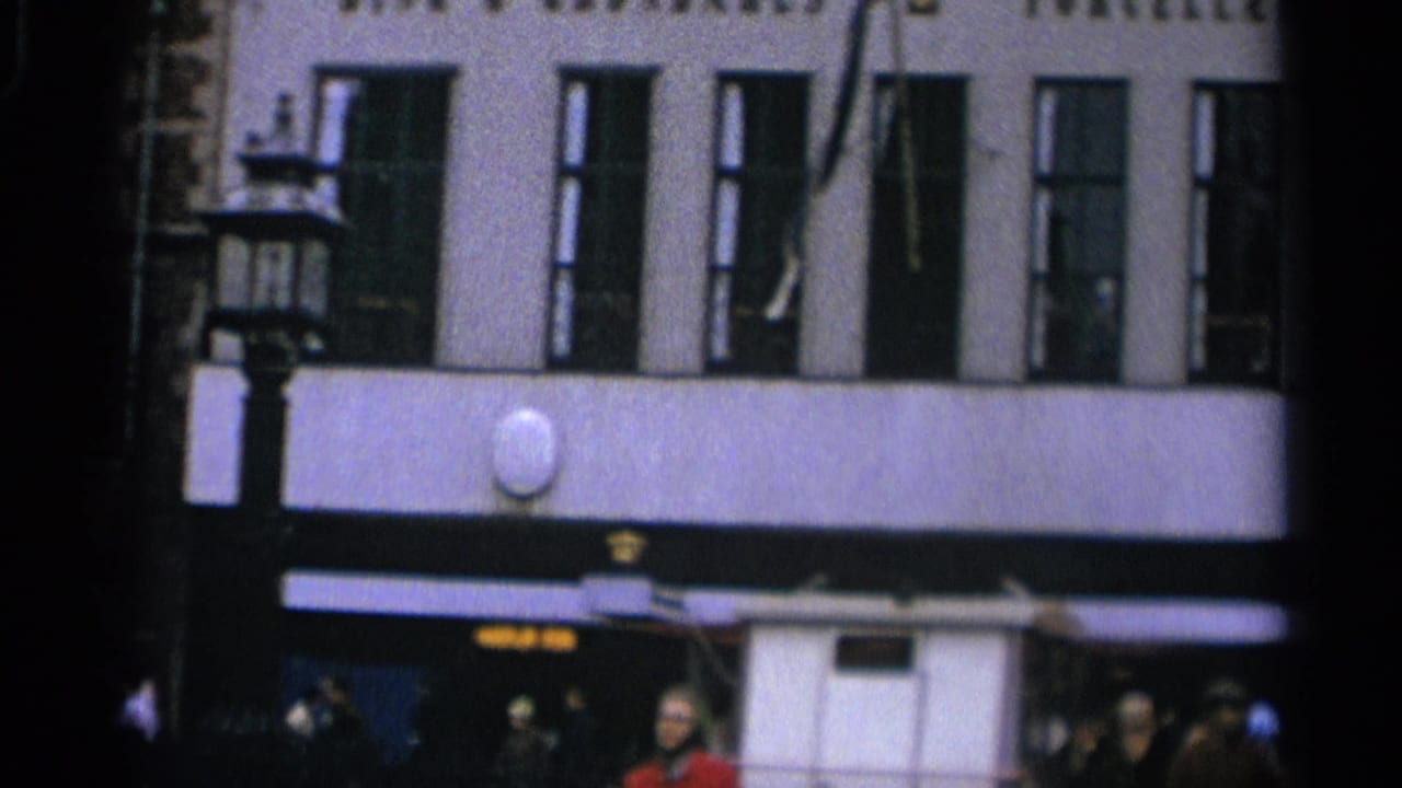 Large building facade with tall windows, awnings, pedestrians, and partial storefront signage.