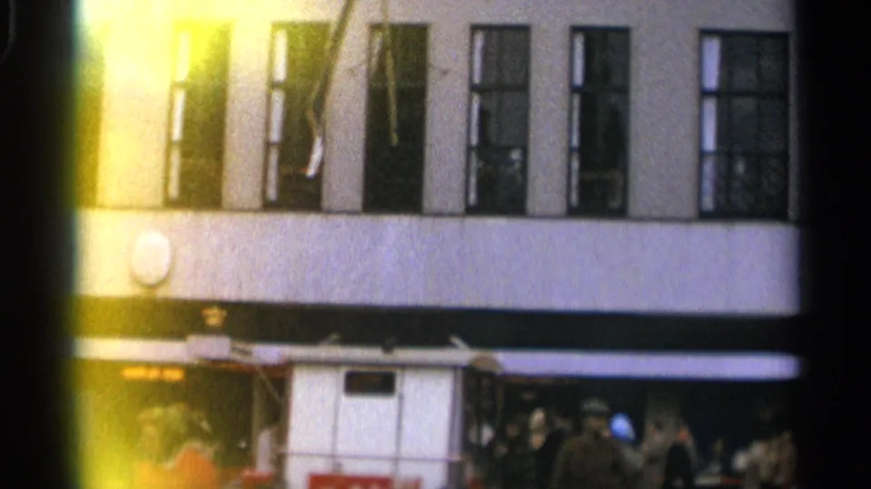 1965 Copenhagen street scene with strong yellow flare at left, tall windows, awnings, and pedestrians gathered near storefronts.