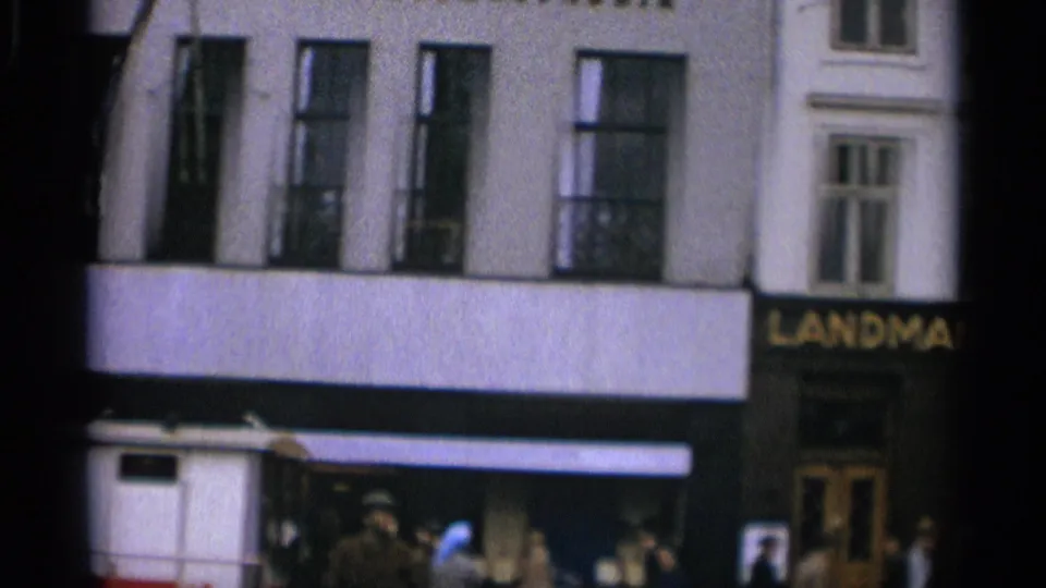 Copenhagen street corner with a pale facade, tall windows, pedestrians, dark awnings, and a visible LANDMAND storefront sign.