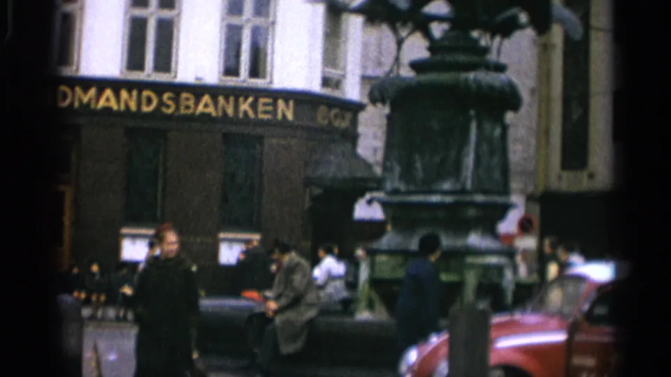 1965 Copenhagen public-square view with a bronze statue in the foreground, Landmandsbanken behind it, pedestrians, and a red car at right.