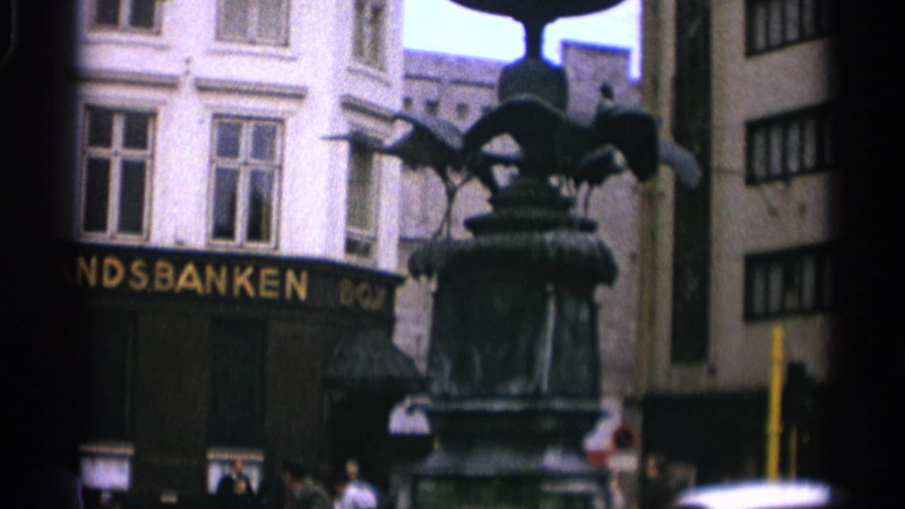 Fountain and partial bank sign seen between city buildings.