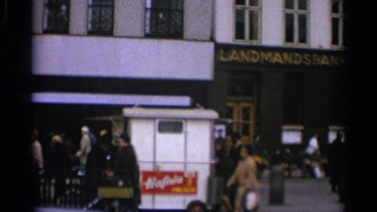 Pedestrians stand and walk near the Landmandsbanken entrance and a small white ice cream cart in Copenhagen.