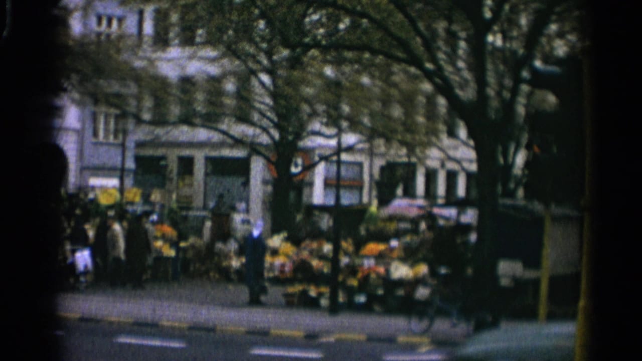 1965 Copenhagen street corner with pedestrians, a flower stall, trees, and building facades seen in soft 8mm color.