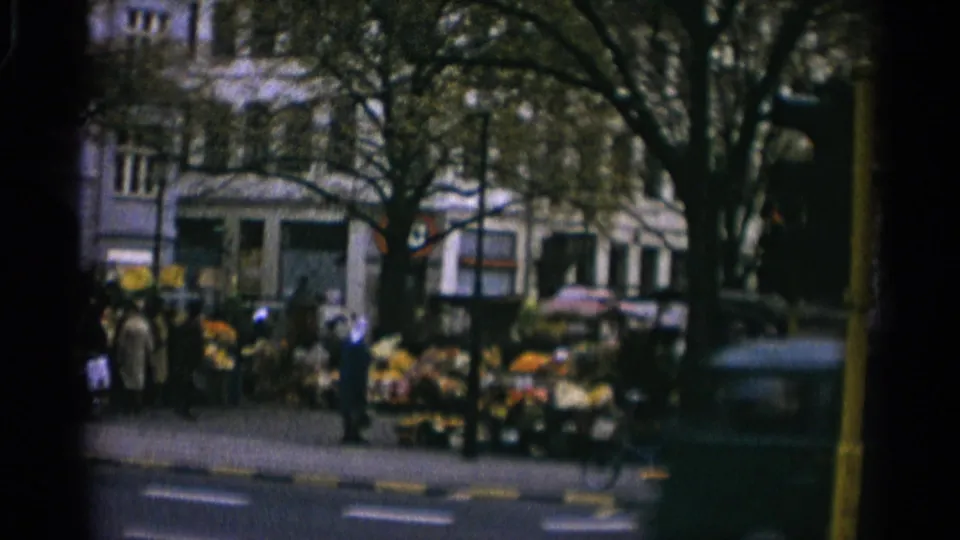 Copenhagen sidewalk scene with people around a flower display, street trees, and mid-century storefronts in the background.