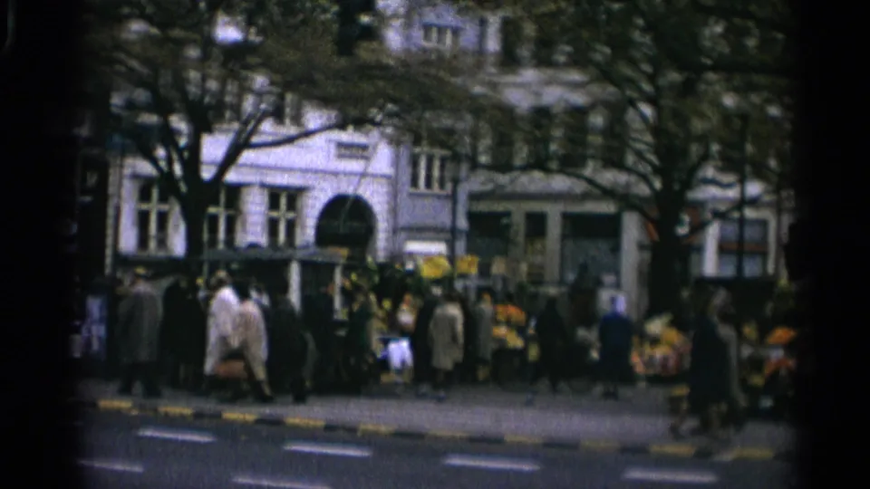 Copenhagen street corner with pedestrians, flower stands, trees, and a large building carrying visible commercial signage.