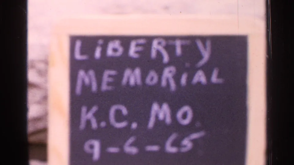 1965 Kansas City home-movie frame showing a handwritten Liberty Memorial K.C. MO. sign with date 9-6-65.