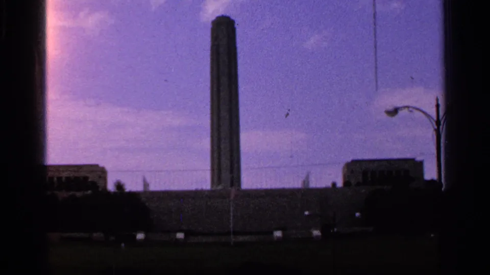 Liberty Memorial tower remains centered in a 1965 Kansas City home-movie view with a streetlamp and low skyline.