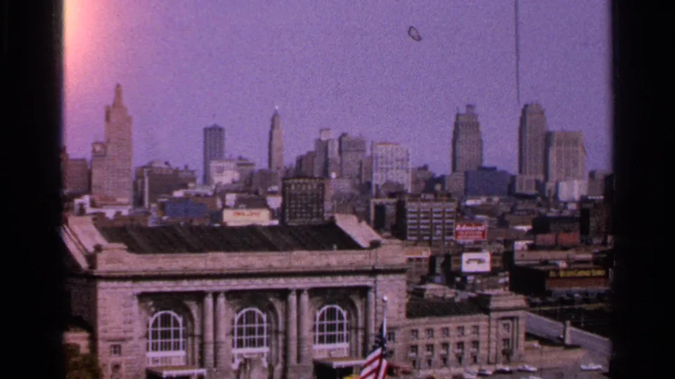 1965 Kansas City skyline view showing downtown towers, rooftop structures, signs, and a civic-style building with arched windows in front.